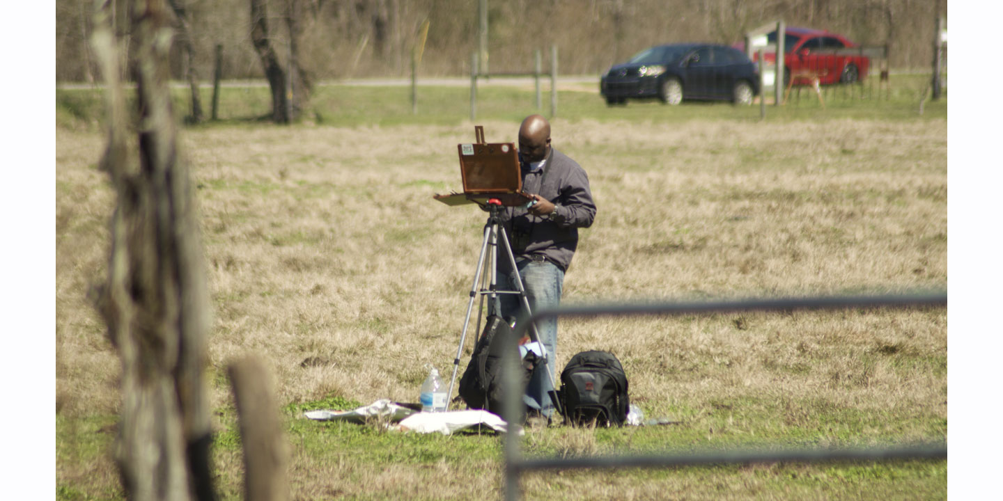 Timothy Joe, wearing a brown shirt standing behind a canvas stand painting bird life at The Joe Farm.